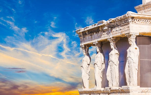 Caryatids of the Erechtheion at Athens Acropolis against a vibrant sky.