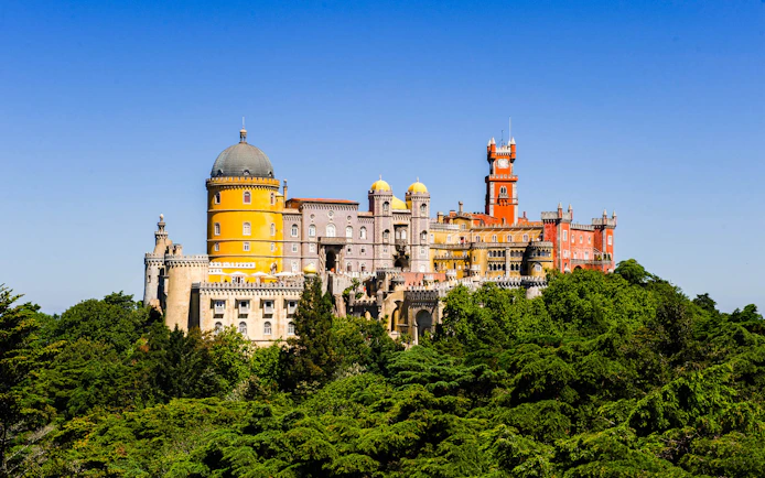 Pena Palace in Sintra surrounded by lush greenery on a clear day.