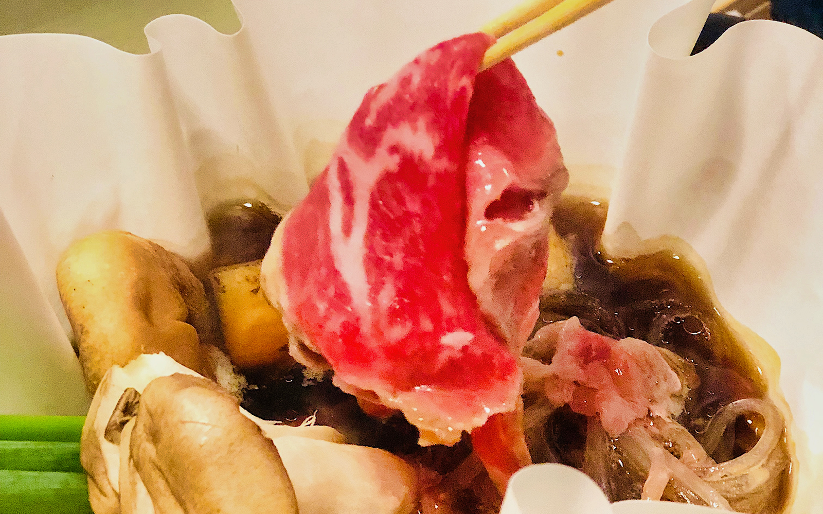 Chopsticks holding marbled beef over hot pot with mushrooms, Kyoto food tour.