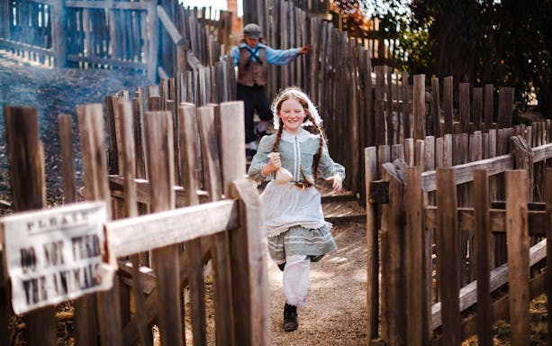 Girl running with a pouch through wooden fences at Sovereign Hill.