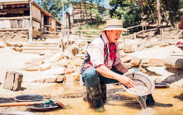 Man panning for gold at Sovereign Hill, Australia, with historic buildings in the background.