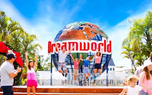 Visitors jumping in front of Dreamworld globe sign, Gold Coast, Australia.