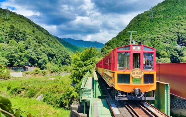 Sagano Romantic Train crossing a bridge through lush green mountains in Kyoto, Japan.