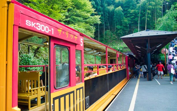 Sagano Romantic Train at station with passengers boarding, surrounded by lush greenery in Kyoto, Japan.