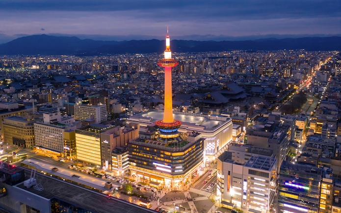 Kyoto Tower illuminated at night with cityscape in the background.