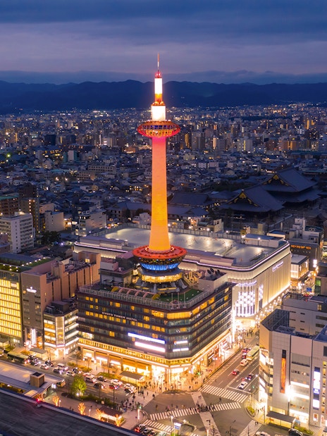 Kyoto Tower illuminated at night with cityscape in the background.