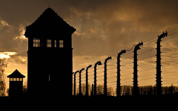 Silhouette of Auschwitz-Birkenau watchtower and barbed wire fence at sunset.