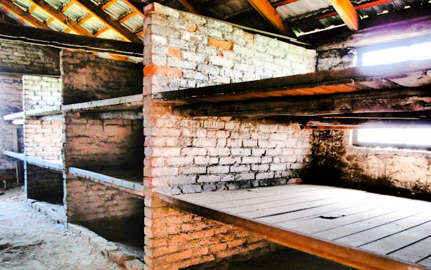 Brick barracks interior at Auschwitz-Birkenau Museum, showcasing wooden bunks.