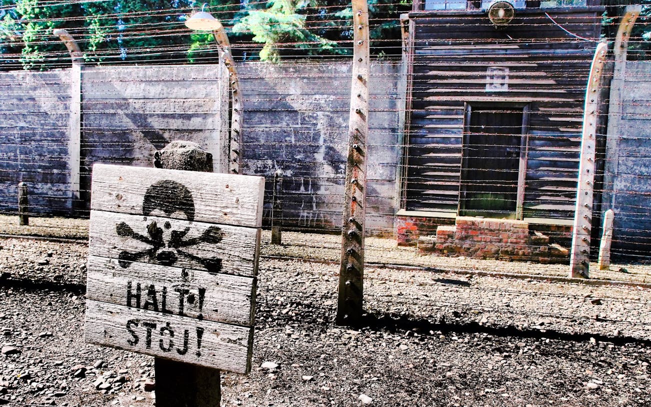 Barbed wire fence and warning sign at Auschwitz-Birkenau Museum.