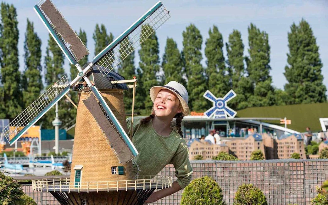 Young girl smiling next to a miniature windmill at Madurodam Miniature Park.