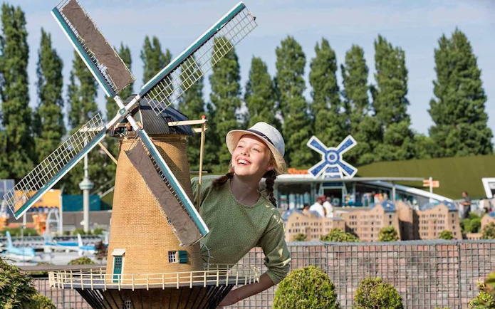 Young girl smiling next to a miniature windmill at Madurodam Miniature Park.