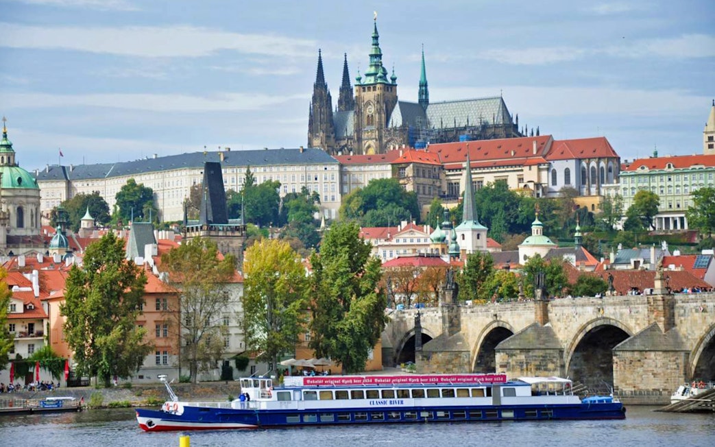 Panoramic view of Prague Castle and Charles Bridge with a cruise boat on the Vltava River.