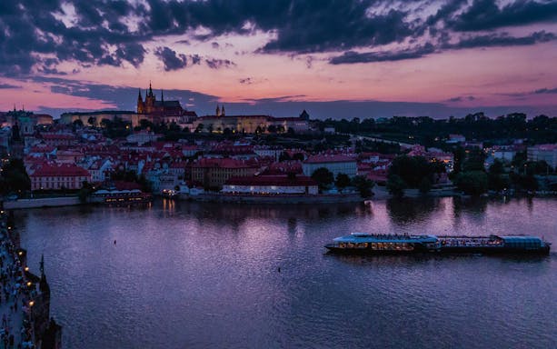 Cruise boat on Vltava River at dusk with Prague Castle in the background.