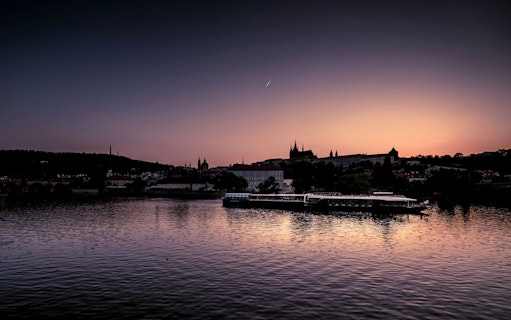 Vltava River cruise at sunset with Prague Castle silhouette.