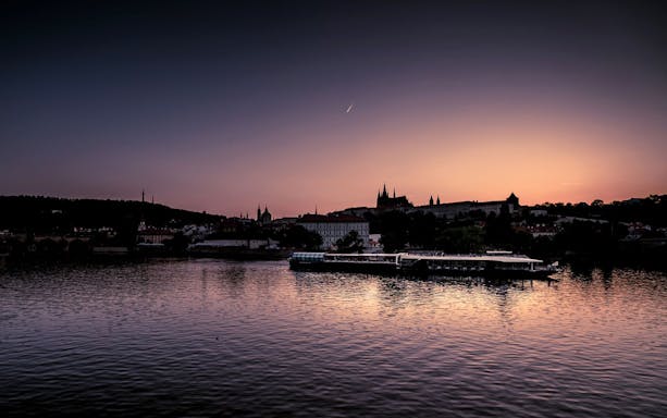 Vltava River cruise at sunset with Prague Castle silhouette.