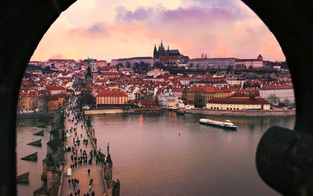 Vltava River cruise boat near Charles Bridge at sunset, Prague skyline in background.