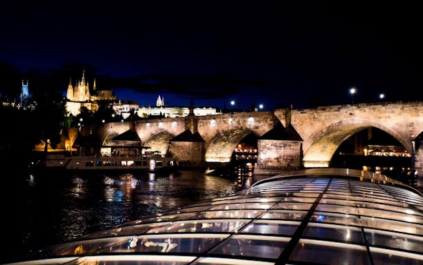 Vltava River cruise at night with view of illuminated Charles Bridge in Prague.