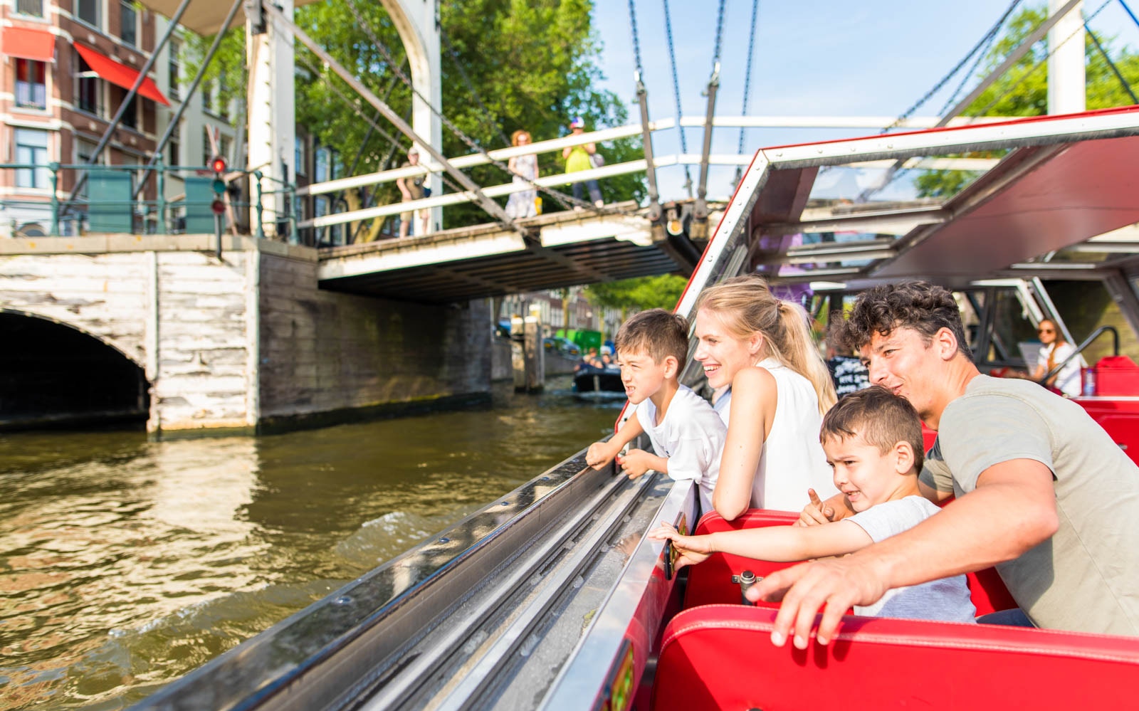 Family enjoying canal boat tour under bridge in Amsterdam.