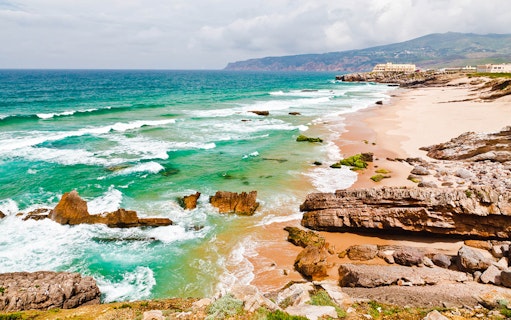 Coastal view of Cabo da Roca with rocky cliffs and turquoise waves near Lisbon.