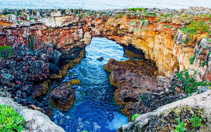 Rocky coastal arch at Cabo da Roca, Portugal, with ocean waves below.