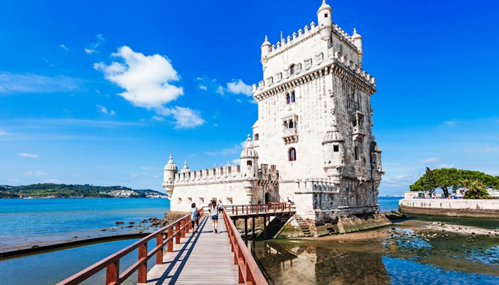 Belém Tower in Lisbon, Portugal, viewed from a wooden walkway over the Tagus River.
