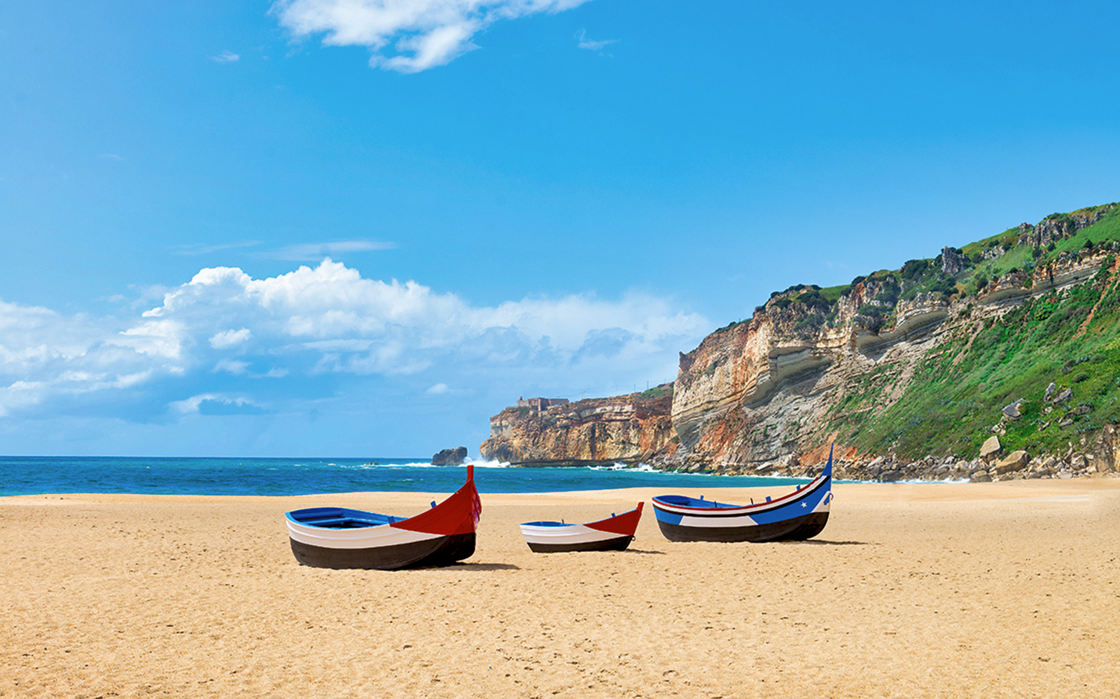 Traditional fishing boats on Nazaré beach with cliffs in the background, Portugal.