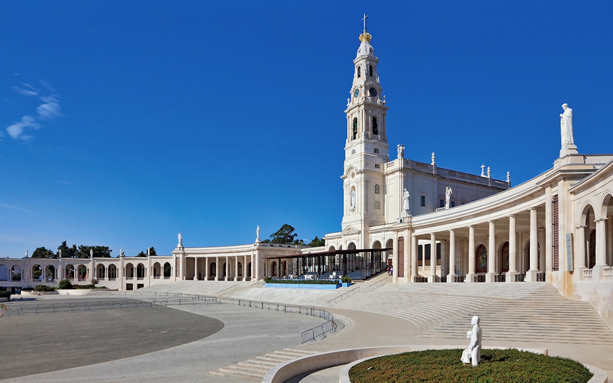 Sanctuary of Fátima with colonnade and basilica under clear blue sky.