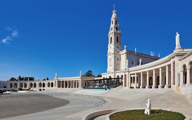 Sanctuary of Fátima with colonnade and basilica under clear blue sky.