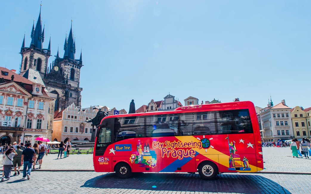 Red City Sightseeing bus in Prague's Old Town Square with Tyn Church in background.