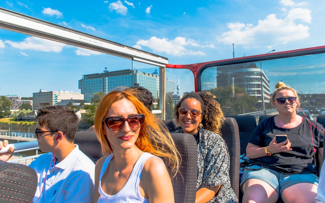 Tourists enjoying a hop-on hop-off bus tour in Prague with cityscape views.