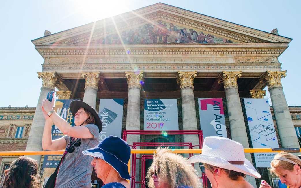 Tourists on a hop-on hop-off bus in front of a historic building in Budapest.
