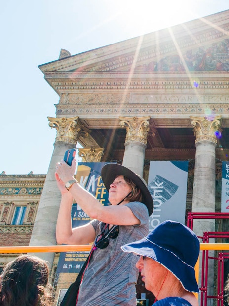 Tourists on a hop-on hop-off bus in front of a historic building in Budapest.