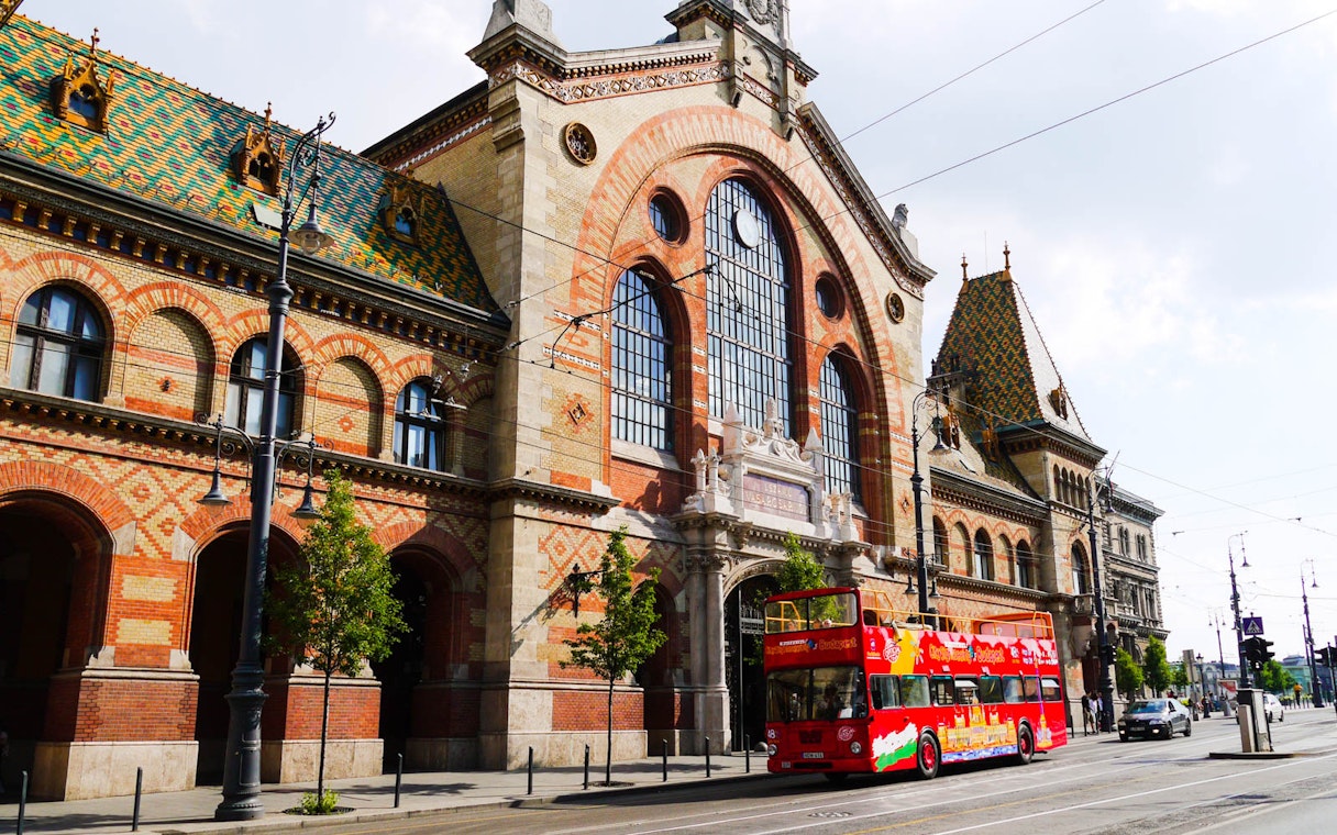 Red double-decker bus in front of Budapest's Great Market Hall on a hop-on hop-off tour.