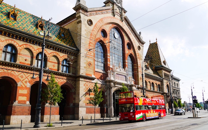 Red double-decker bus in front of Budapest's Great Market Hall on a hop-on hop-off tour.
