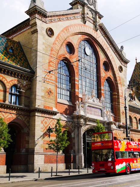 Red double-decker bus in front of Budapest's Great Market Hall on a hop-on hop-off tour.