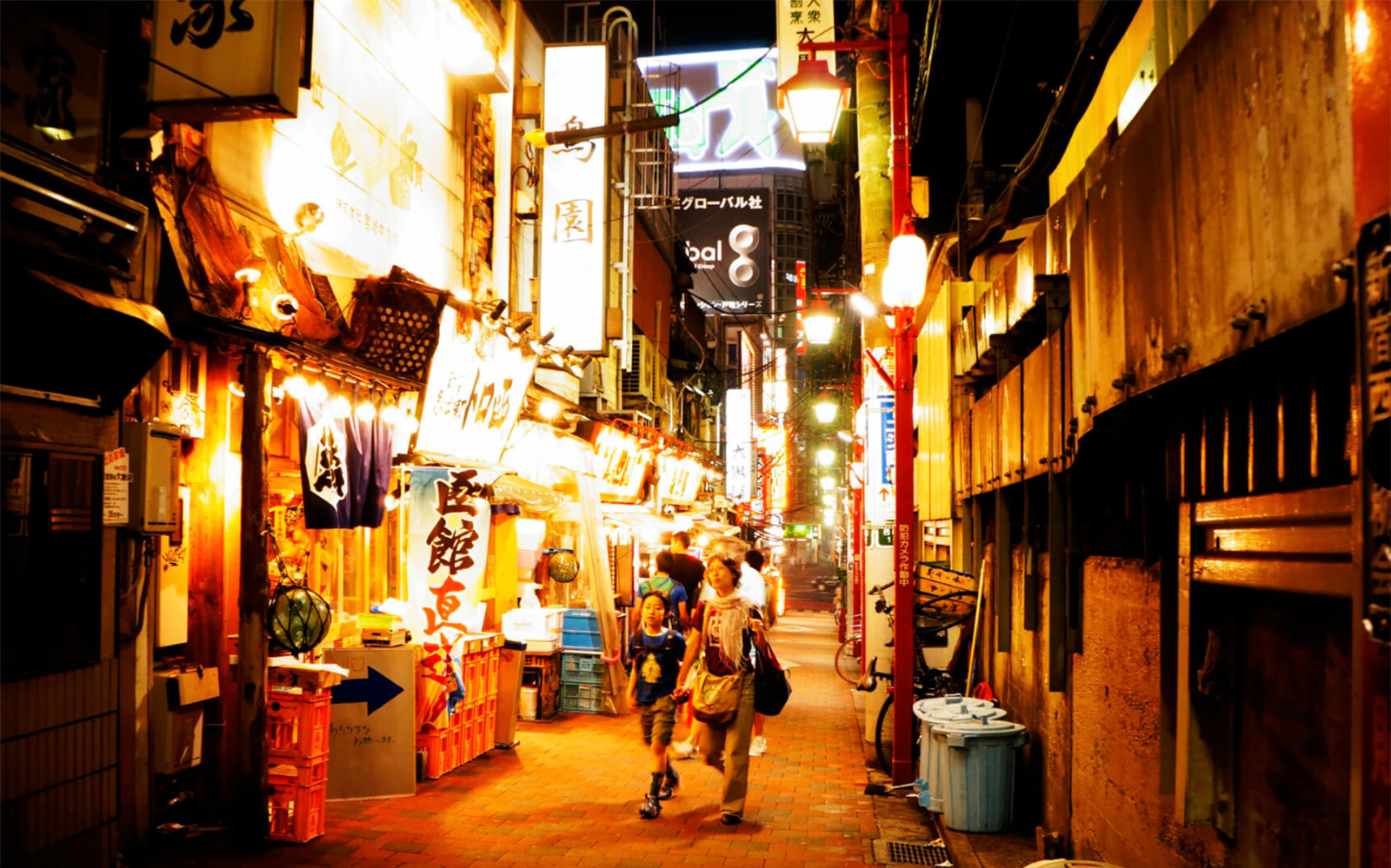 Shinjuku Omoide Yokocho alley with illuminated signs and people walking at night.