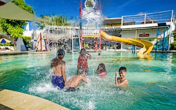Children playing under a water feature at Splash Waterpark with slides in the background.