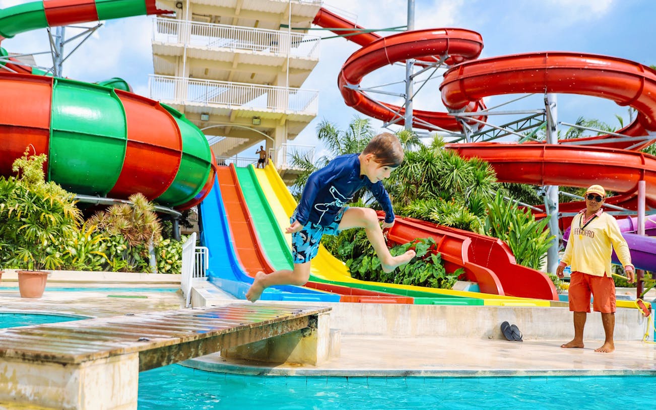 Child jumping into pool at Splash Waterpark with colorful slides in background.