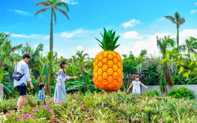 Family exploring Nago Pineapple Park with large pineapple sculpture.