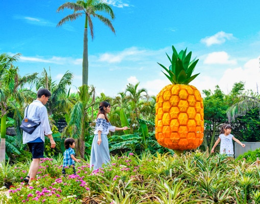 Family exploring Nago Pineapple Park with large pineapple sculpture.