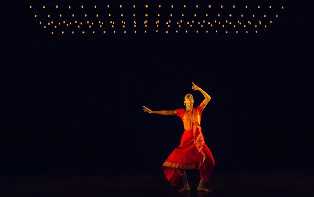 Dancer in red performing under dim lights, Akram Khan Company – We are but Shadows.