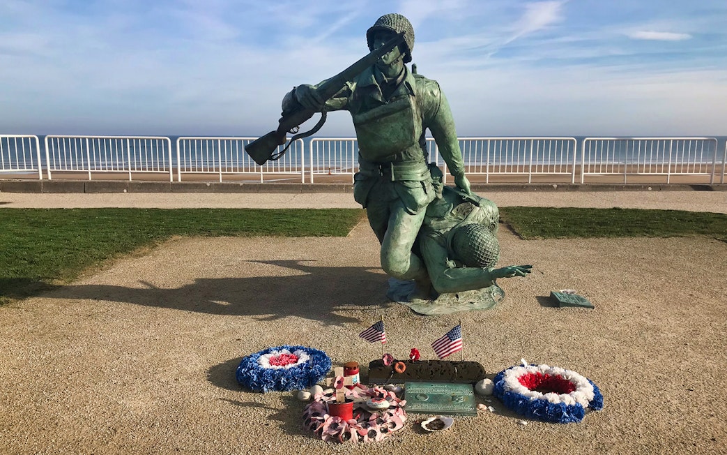 Normandy D-Day memorial statue with wreaths and flags at Omaha Beach.