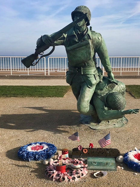 Normandy D-Day memorial statue with wreaths and flags at Omaha Beach.
