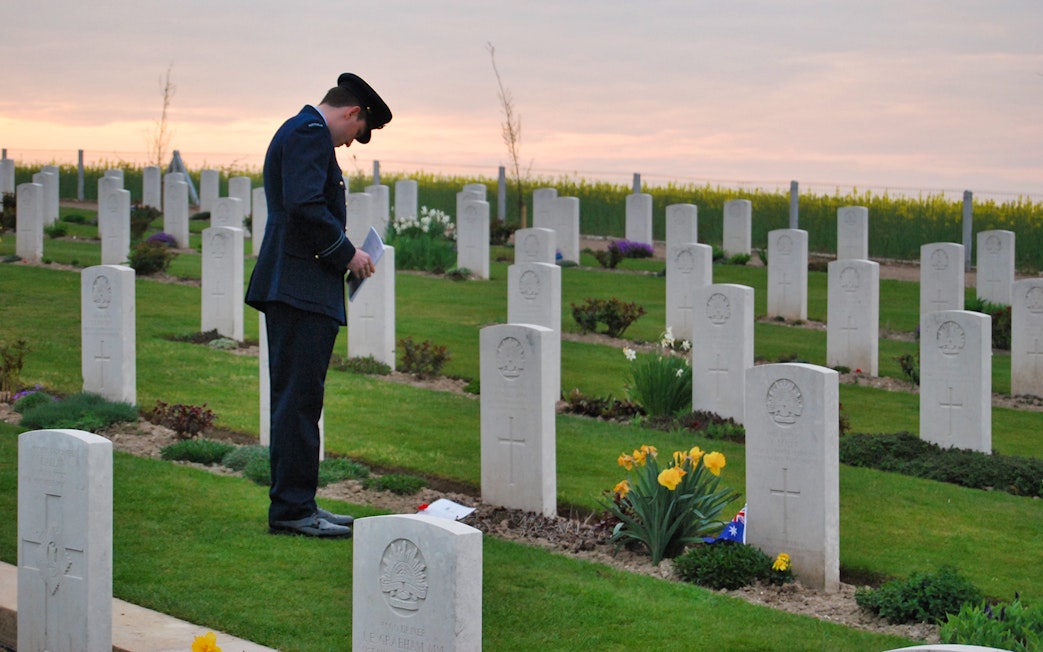 Man in uniform paying respects at Normandy D-Day cemetery at sunset.