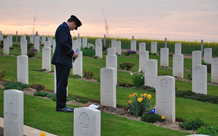 Man in uniform paying respects at Normandy D-Day cemetery at sunset.