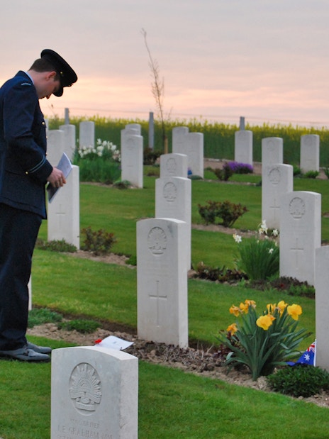 Man in uniform paying respects at Normandy D-Day cemetery at sunset.
