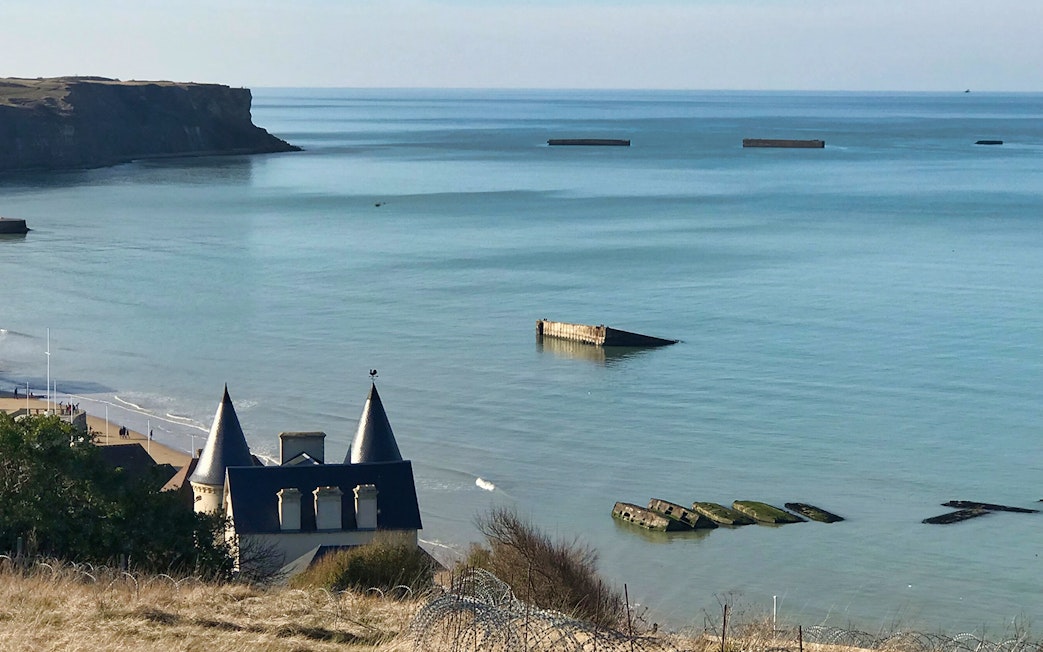 Normandy D-Day landing beach with remnants of Mulberry Harbor in the sea.