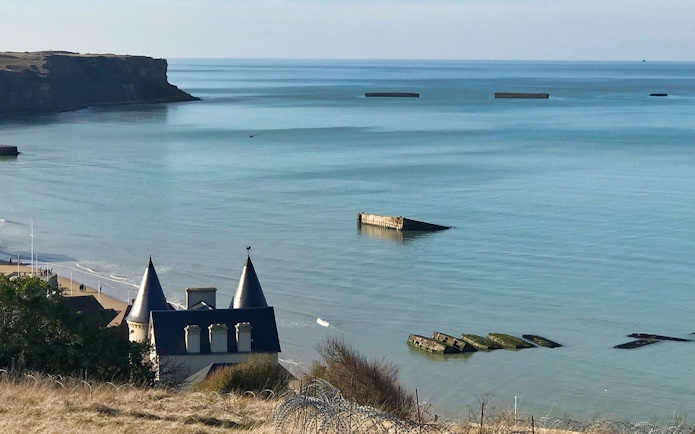 Normandy D-Day landing beach with remnants of Mulberry Harbor in the sea.