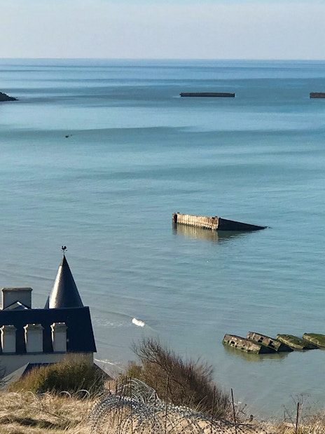 Normandy D-Day landing beach with remnants of Mulberry Harbor in the sea.