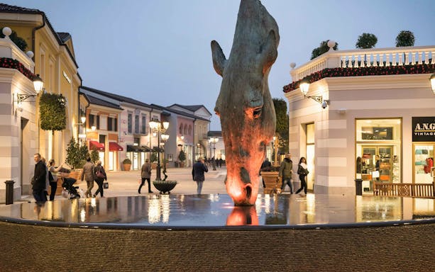 Serravalle Designer Outlet with horse sculpture and shoppers, transport from Milan.